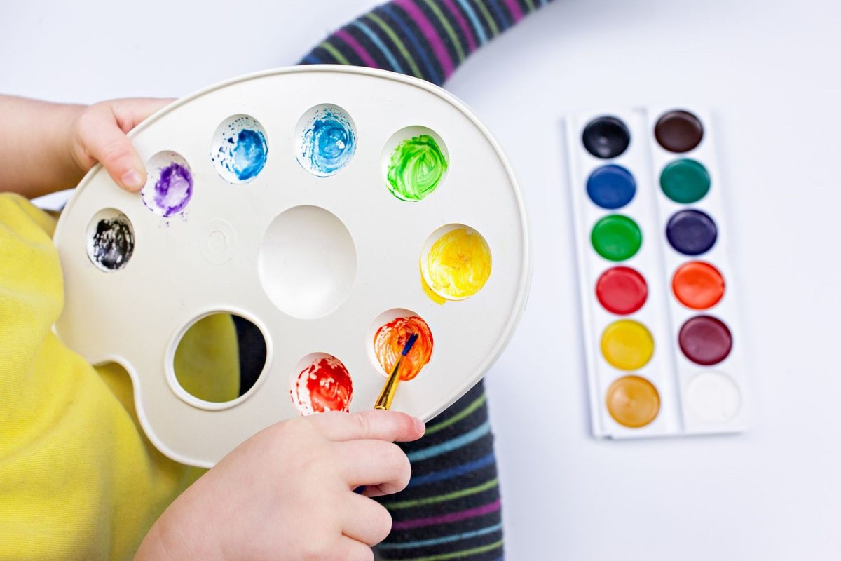 Enfant tenant une palette de peinture avec pinceau au-dessus d'une palette de couleurs Enfant tenant une palette de peinture avec pinceau au-dessus d'une palette de couleurs