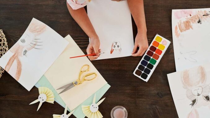 Person dessinant des lapins avec des crayons et des aquarelles sur une table en bois