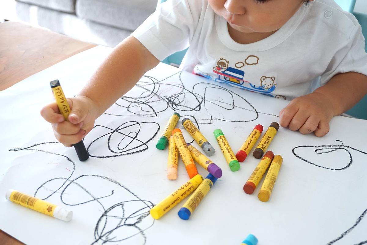 Un enfant dessine des formes libres avec des crayons gras Un enfant dessine des formes libres avec des crayons gras