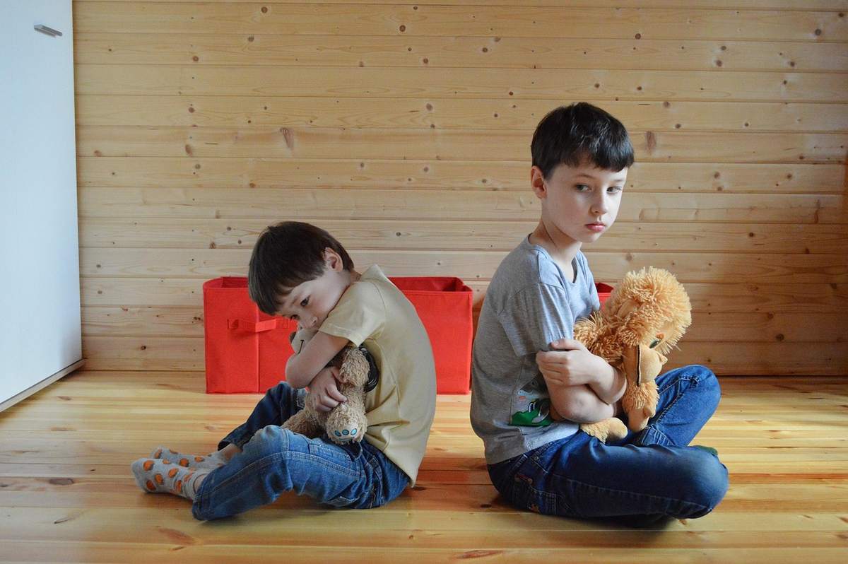 Deux garçons assis dos à dos, chacun serrant un ours en peluche Deux garçons assis dos à dos, chacun serrant un ours en peluche