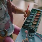 Enfant avec pinceau, peintures, et objets sur une table