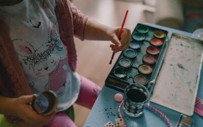 Enfant avec pinceau, peintures, et objets sur une table