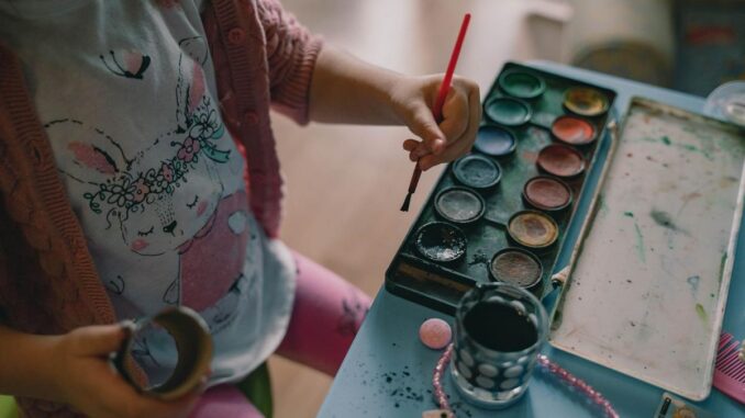 Enfant avec pinceau, peintures, et objets sur une table