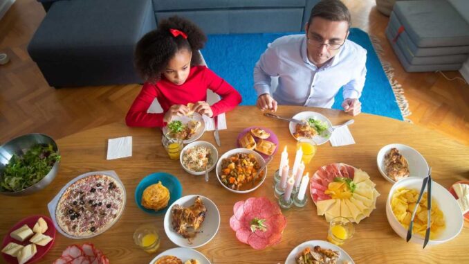 Famille partageant un repas de pâques avec divers plats sur une table en bois dans un salon