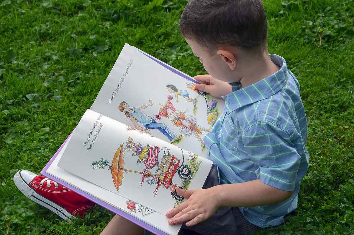 Un garçon assis sur l'herbe lit un livre illustré coloré Un garçon assis sur l'herbe lit un livre illustré coloré