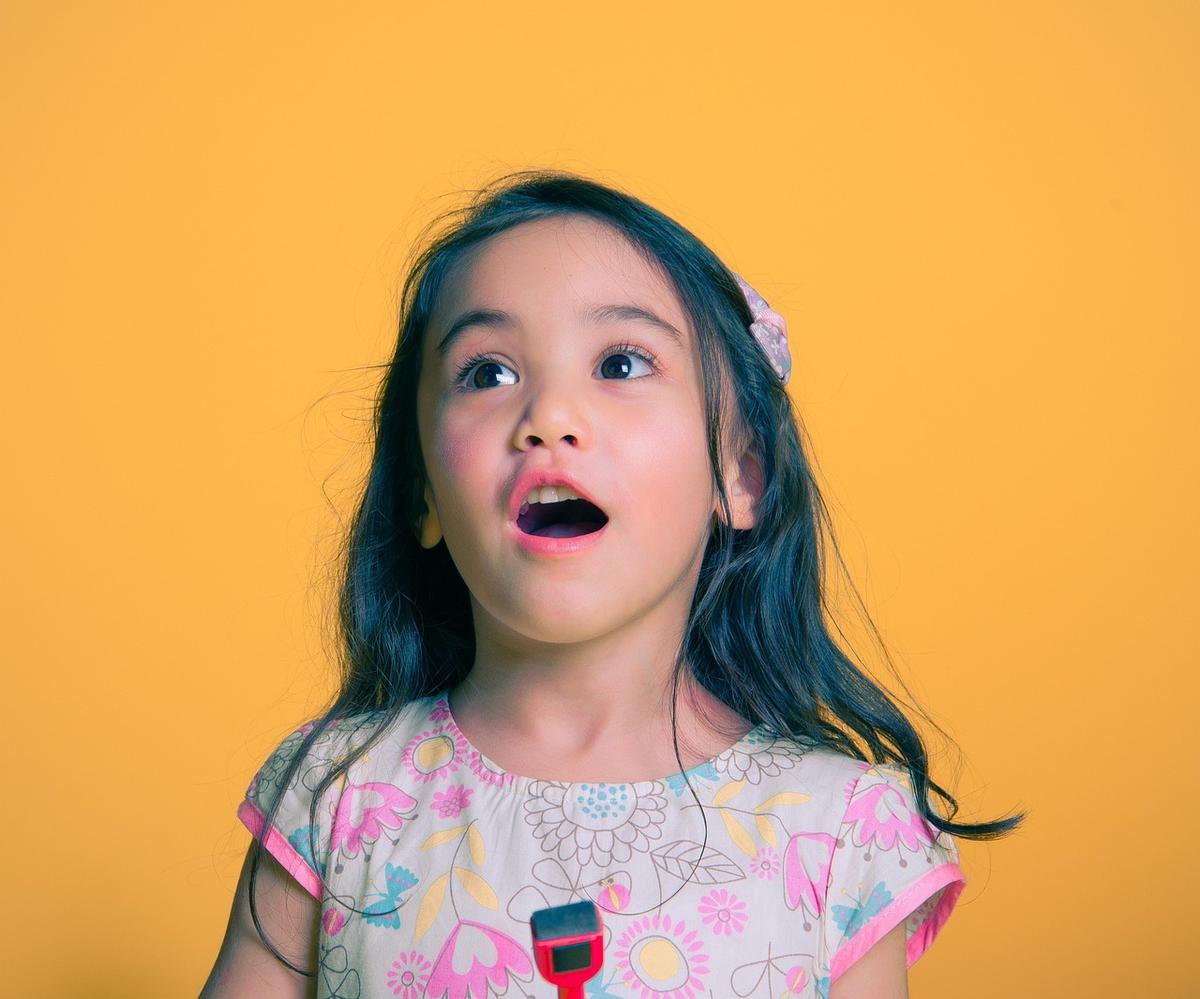 Une petite fille aux cheveux noirs regarde en haut, bouche ouverte Une petite fille aux cheveux noirs regarde en haut, bouche ouverte