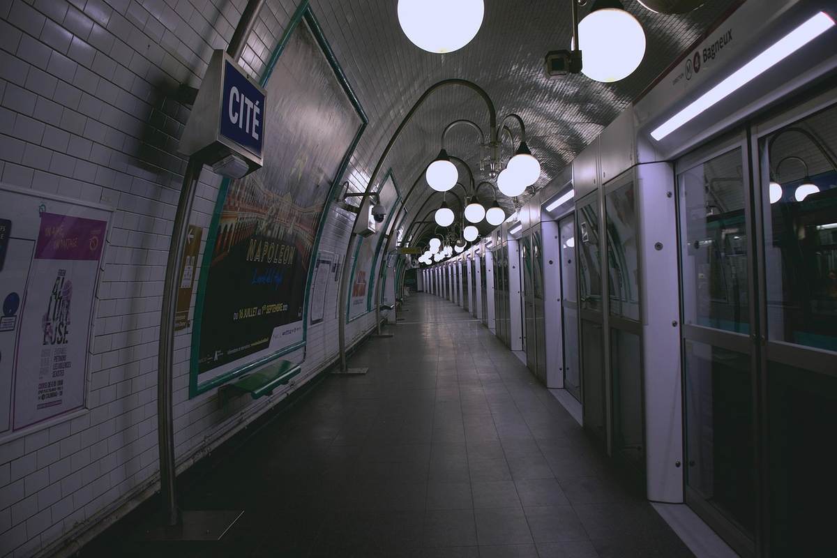 Couloir souterrain de station de métro parisien désert, illuminé par des lampadaires, panneaux publicitaires sur les murs Couloir souterrain de station de métro parisien désert, illuminé par des lampadaires, panneaux publicitaires sur les murs
