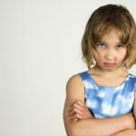 Une enfant sérieuse aux cheveux courts serre les bras contre un fond blanc