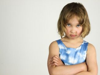 Une enfant sérieuse aux cheveux courts serre les bras contre un fond blanc