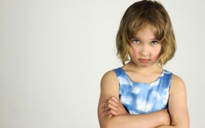 Une enfant sérieuse aux cheveux courts serre les bras contre un fond blanc