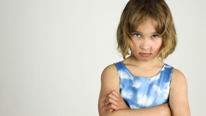 Une enfant sérieuse aux cheveux courts serre les bras contre un fond blanc