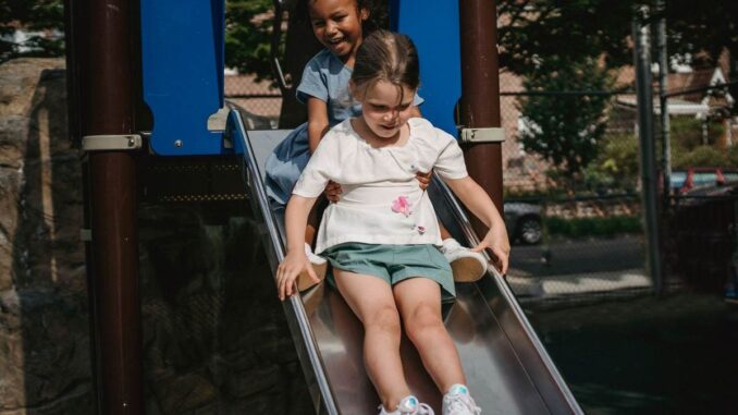 Enfants sur une glissière dans un parc, structures bleues et végétation environnante