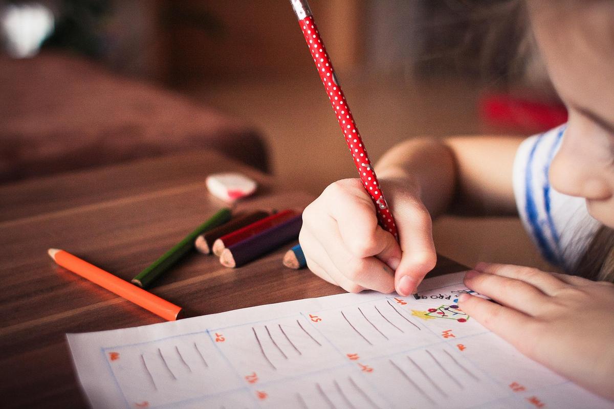 Un enfant trace des lignes avec un crayon rouge sur une feuille