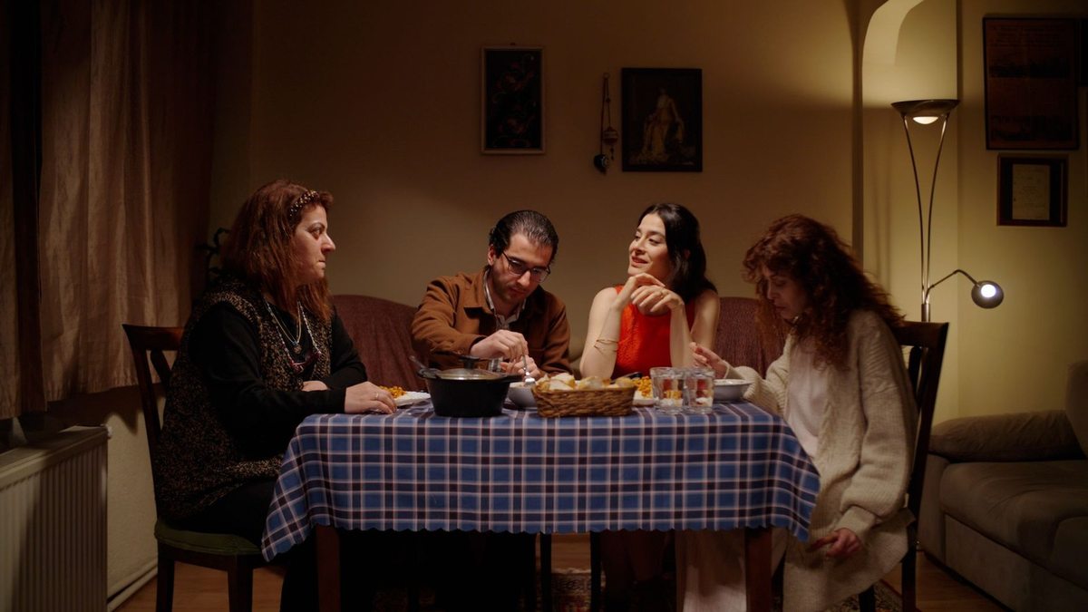 Quatre individus assis autour d'une table à motifs bleu et blanc dans une pièce décorée de cadres
