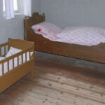 Chambre aménagée avec un lit adulte et un petit berceau en bois clair pour enfant