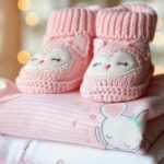 Chaussons tricotés roses et bodies pastel empilés, décor lumineux