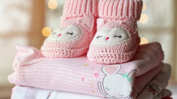 Chaussons tricotés roses et bodies pastel empilés, décor lumineux