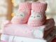 Chaussons tricotés roses et bodies pastel empilés, décor lumineux